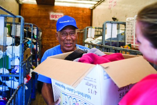 Goodwil trailer attendant is smiling and accepting a box of donations from someone.