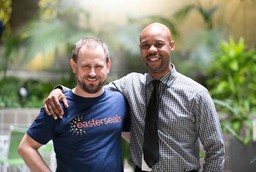White man with blue Easterseals t-shirt has arm around African American man in patterned shirt and black tie
