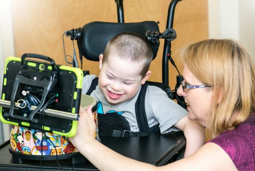 Young boy in wheelchair laughing, using drum technology with therapist helping
